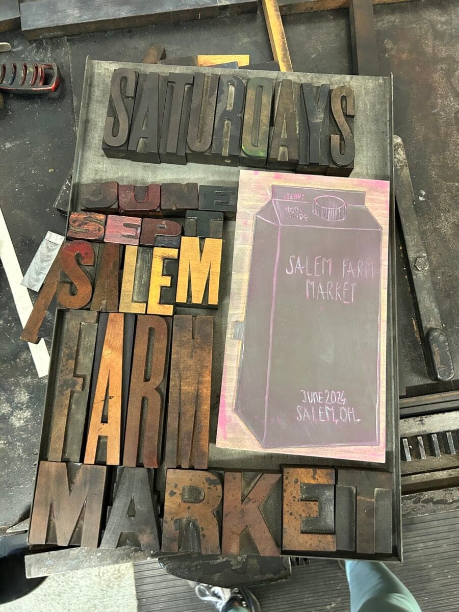 Wooden letterpress type spelling "Saturdays Salem Farm Market" is arranged next to a pink chalk drawing on a blackboard showing "Salem Farm Market June 2024, Salem, OH.