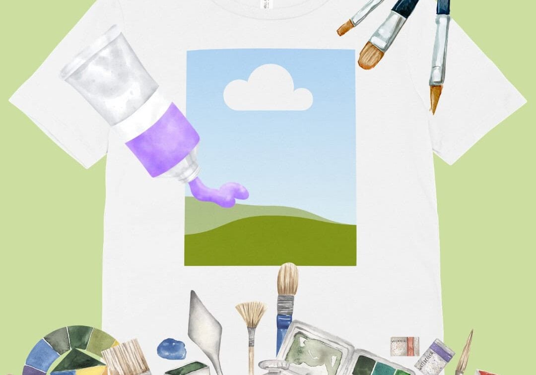 A white T-shirt with a simple landscape and cloud graphic, surrounded by watercolor art supplies, including paint tubes, palettes, brushes, and spatulas, on a light green background.